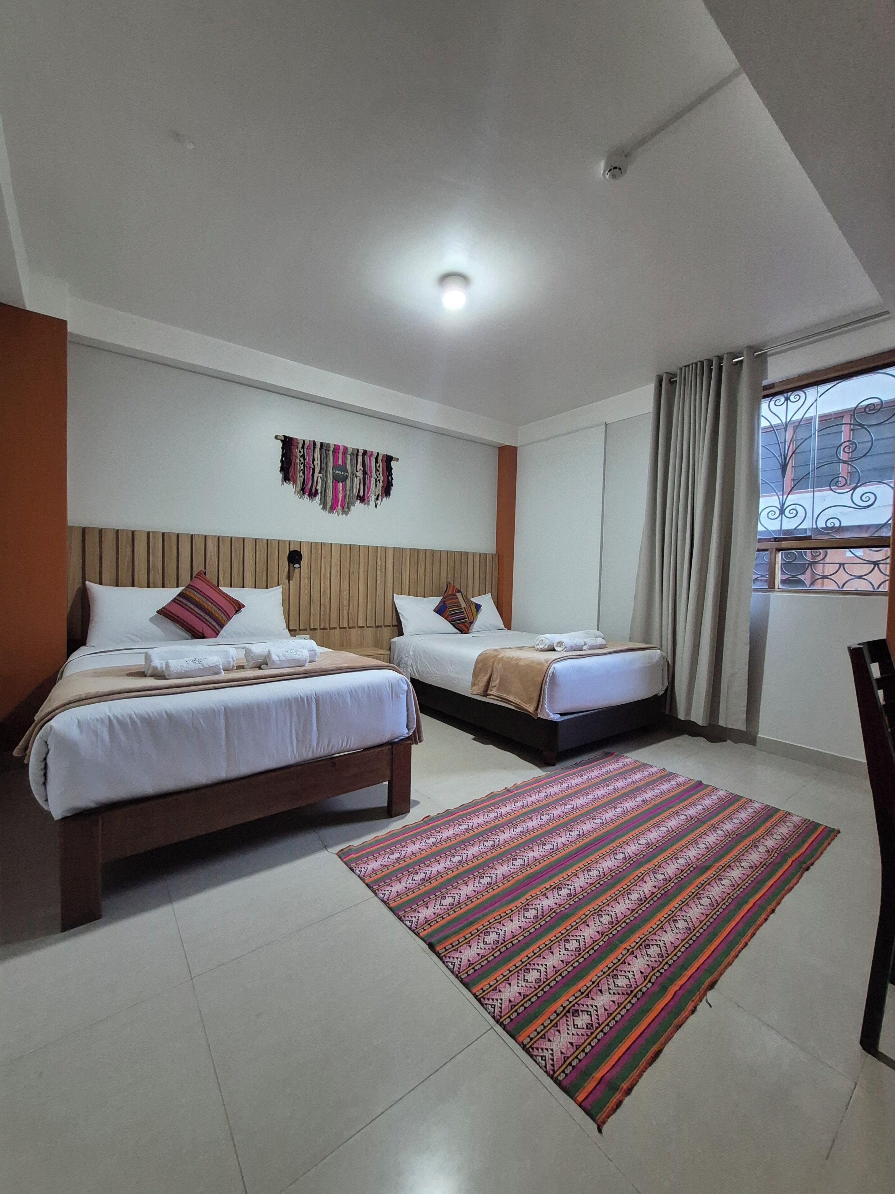 A hotel room with two beds, a patterned rug, a wooden headboard, and a view of the outside.