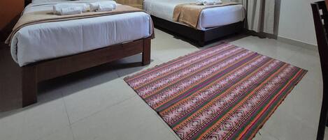 Habitación de hotel con dos camas, un tapete estampado, cabecera de madera y vistas al exterior.