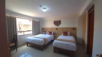 A hotel room with two beds, a ceiling light, a window with curtains, and a wall-mounted decoration.