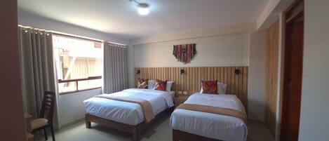 A hotel room with two beds, a ceiling light, a window with curtains, and a wall-mounted decoration.