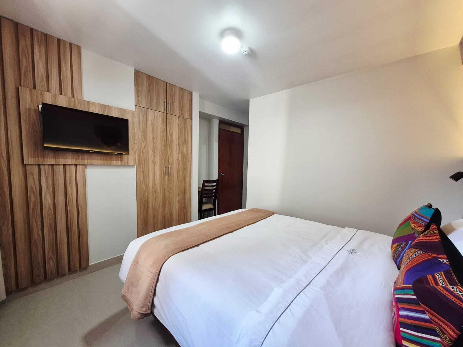 A bedroom with a bed, a TV mounted on the wall, and a door leading to another room.