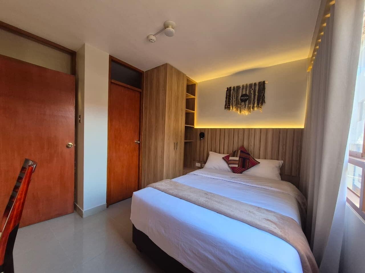 A bedroom with a bed, wooden wardrobe, and a ceiling light fixture.