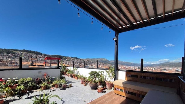 A rooftop terrace with potted plants, a wooden deck, and a view of a cityscape. - Adolfos Hotel Cusco (Cusco)