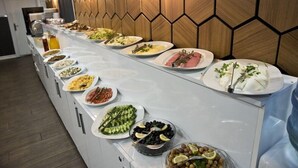 Buffet com diversos pratos e parede de madeira com padrão geométrico.