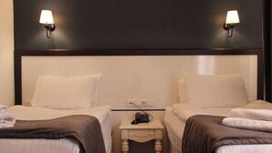 Quarto de hotel com duas camas, uma mesa de cabeceira com telefone e luminárias fixadas na parede.