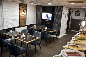 Un restaurante con pared de ladrillo, una pantalla de televisión y un bufé con diversos platos.