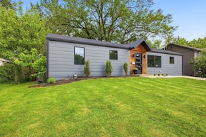 A modern two-story house with a well-maintained lawn, a small garden, and a large tree in the background.