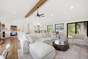 A modern living room with a sectional sofa, a coffee table, and a dining area with a kitchen in the background.