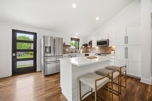 A modern kitchen with a central island, stainless steel appliances, and a view through a door.