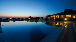 Un'area piscina tranquilla al crepuscolo, con cielo sereno, un edificio ben illuminato e sedie a sdraio.
