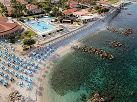 Un complejo turístico frente al mar con piscina, sombrillas de playa y aguas cristalinas.