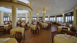 Un'ampia sala da pranzo con diversi tavoli e sedie, grandi finestre e un soffitto alto.