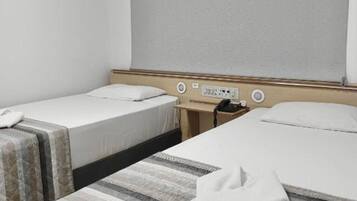 Quarto de hotel com duas camas, uma janela com persiana, um ar condicionado e uma mesa de cabeceira com telefone.