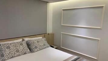 Quarto de hotel com cama, almofadas, mesa de cabeceira e luminária na parede.