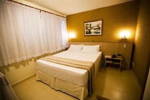 A hotel room with a bed, a nightstand, a painting, and a window with curtains. - Harbor Self Cidade Verde (Maringá)