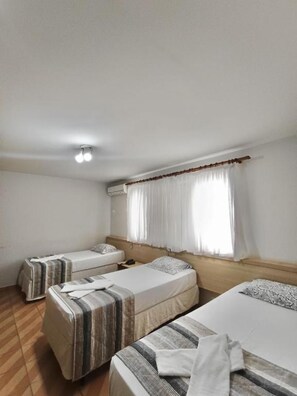 A hotel room with three single beds, a window with curtains, an air conditioning unit, and a wooden floor. - Harbor Self Cidade Verde (Maringá)