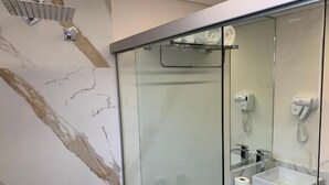Un baño moderno con ducha de vidrio, lavamanos blanco y un perchero para toallas.