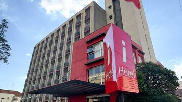 A multi-story hotel with a prominent red and white sign, a covered entrance, and a parking lot.