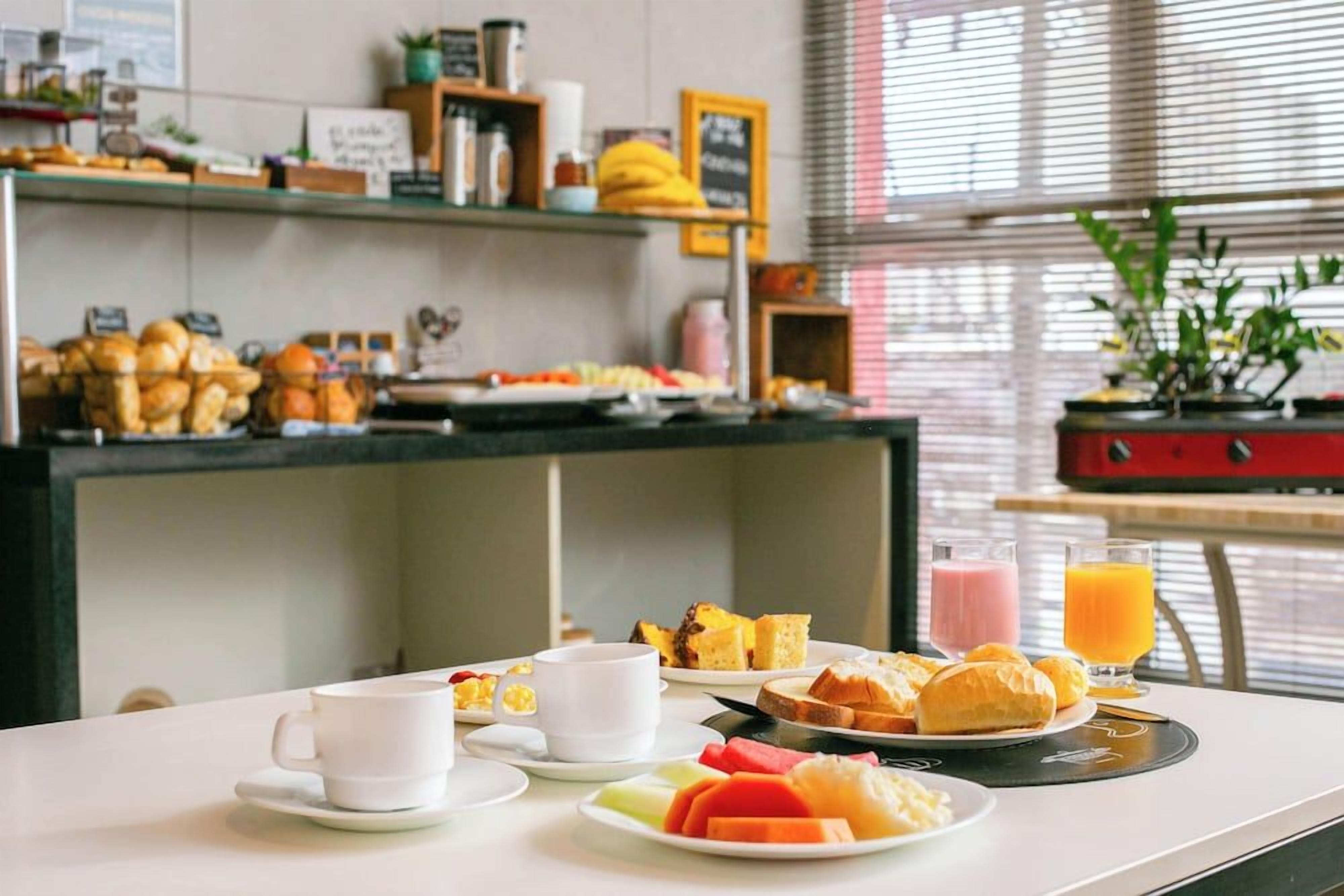 Um buffet de café da manhã com diversos pães, frutas e bebidas.