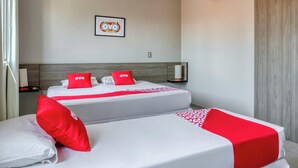 Habitación de hotel con dos camas, cada una con ropa de cama blanca y detalles rojos, un cuadro en la pared y una mesita de noche con una lámpara.