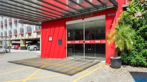 Un edificio rojo con entrada de vidrio, zona de estacionamiento y un cartel que indica 'OYO HOTEL'.