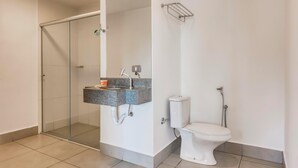 Un baño moderno con cabina de ducha de vidrio, lavabo con encimera de granito, inodoro y toallero.