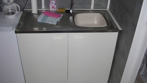 A kitchen with a sink, cabinets, a coffee maker, and cleaning supplies.