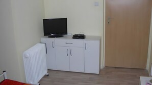 A room with a white cabinet, a television on top, a radiator, and a wooden door.
