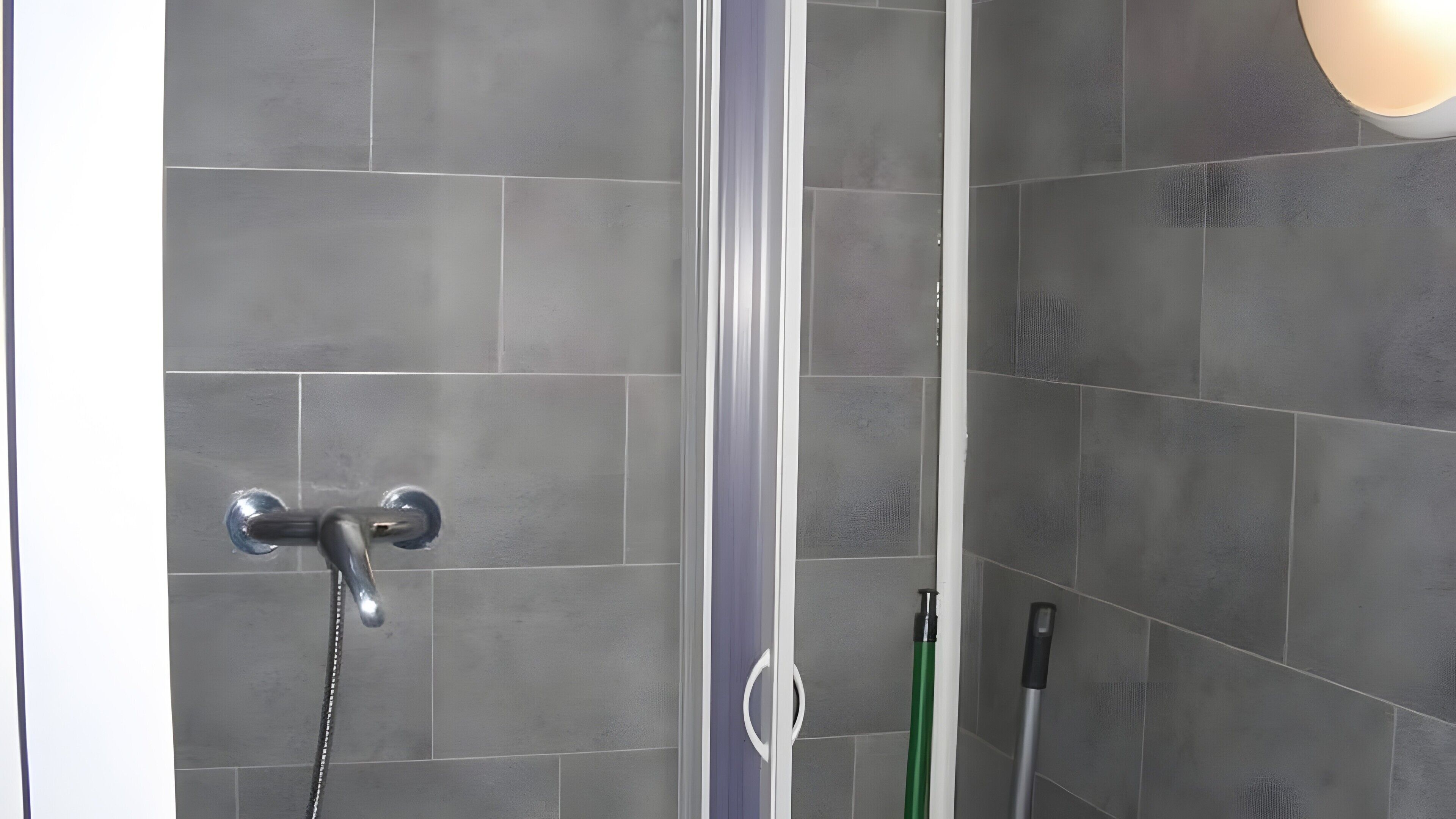 A shower area with grey tiles, a showerhead, and a green cleaning tool.