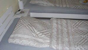 A bed with a white knitted blanket, a bedside table with a lamp, and a wall socket.