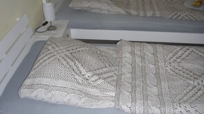 A bed with a white knitted blanket, a bedside table with a lamp, and a wall socket. - Apartment for 2 Guests (20 m²) with Shared Garden and Wi-Fi (Künzell)
