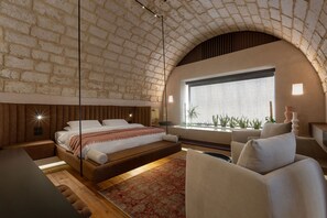 Un dormitorio con techo de ladrillo, un ventanal con plantas, una cama y una zona de estar.