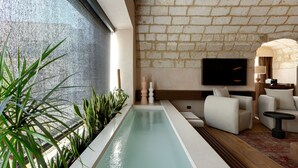 A modern indoor pool area with a stone wall, a flat-screen TV, and a seating area with sofas and a small table. - MBH | Tobacco Deluxe Room (Diso Spongano)
