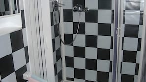 A bathroom with a checkered floor, a shower with a glass door, and a white sink. - Studio Apartment for 2, 18 m², with Shared Garden and Wi-Fi (Künzell)