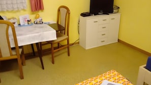 A room with a dining table, chairs, a television on a cabinet, and a patterned rug. - Studio Apartment for 2, 18 m², with Shared Garden and Wi-Fi (Künzell)
