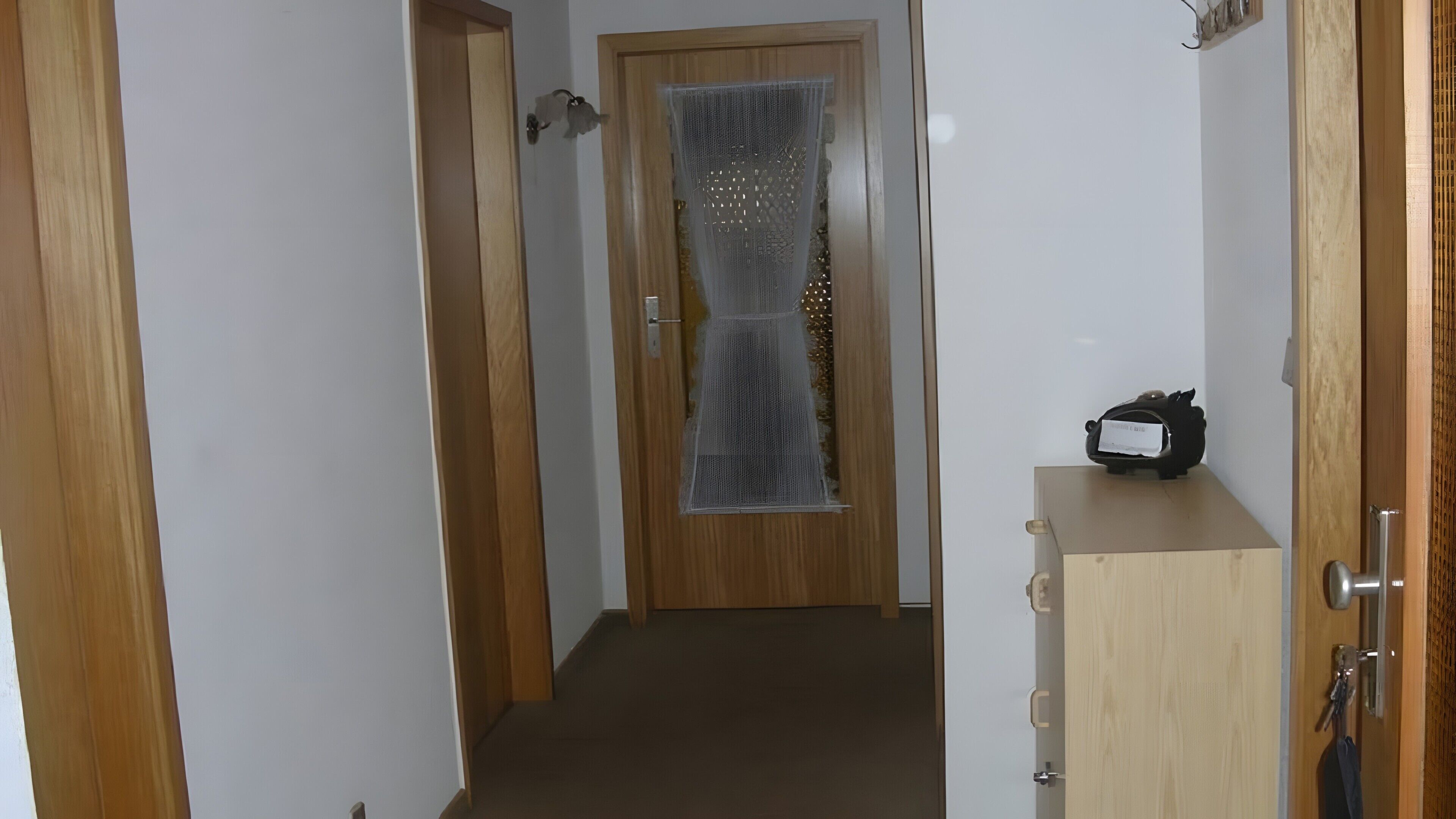 Un pasillo con una puerta de madera, un armario pequeño y un abrigo colgado en la puerta.