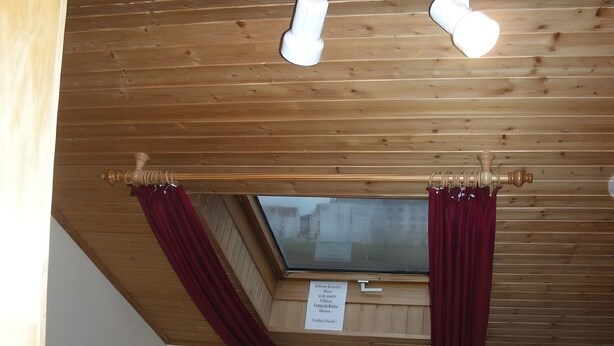 Ett rum med träpanel i taket, ett fönster med gardiner och en skylt på väggen.
