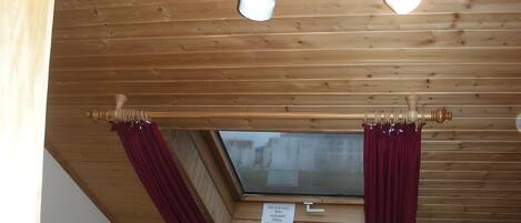 A room with wooden panel ceilings, a window with curtains, and a sign on the wall.