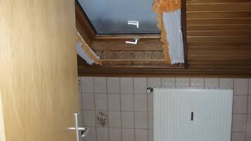 A room with a tiled wall, a white door, and a partially damaged ceiling.