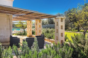 Eine Terrasse im Freien mit Korbmöbeln, einer Pergola und Blick auf einen Swimmingpool.
