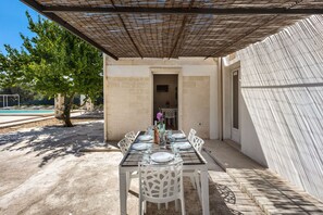 Un área de comedor al aire libre con una pérgola, paredes de piedra y una piscina al fondo.
