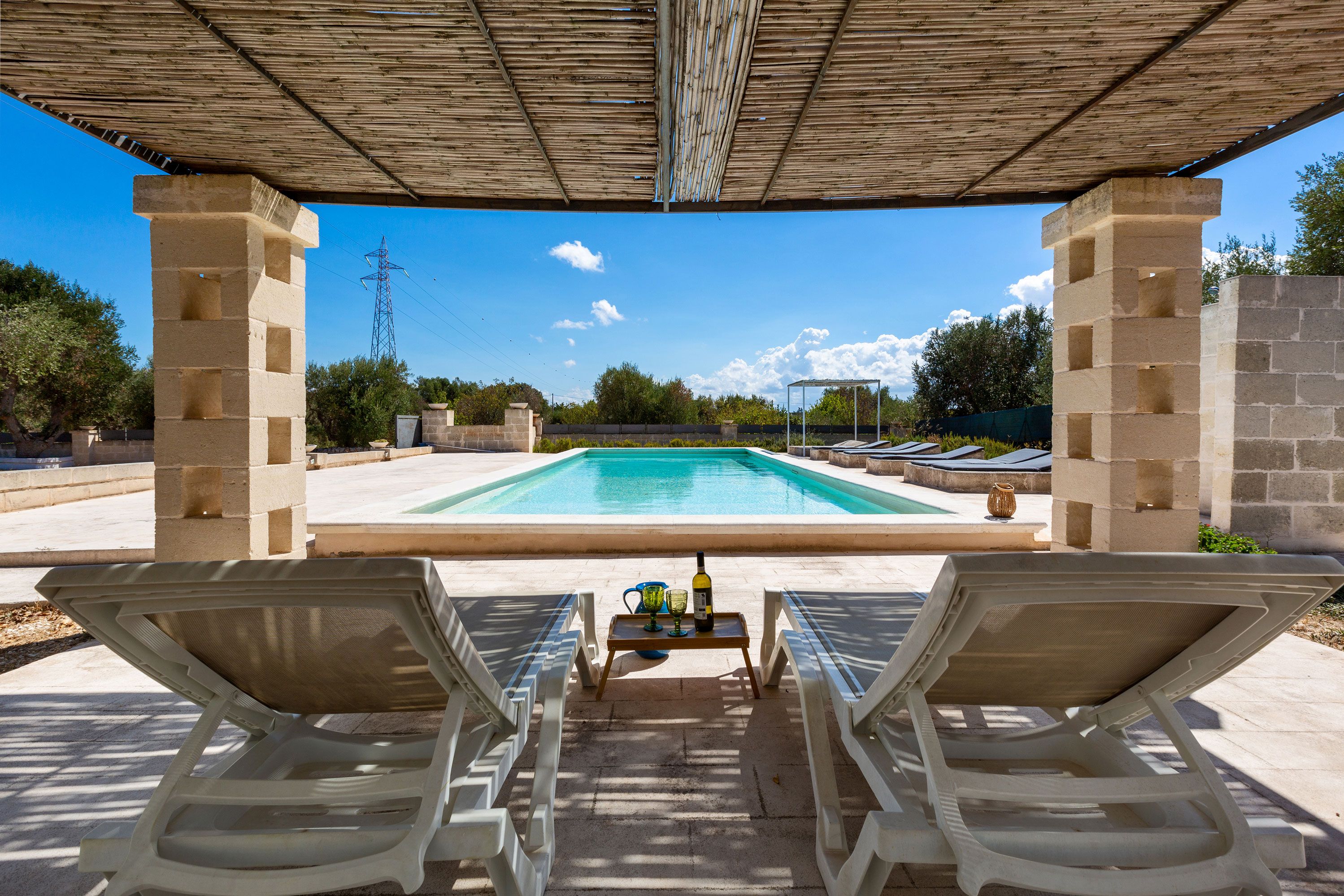 Ein Poolbereich mit zwei Liegestühlen, einem Tisch mit Flasche und Gläsern und freiem Blick auf den Pool.