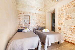 A room with two beds, a stone wall, a small mirror, and a lamp. - Villa Santa Lucia by Perle di Puglia (Ostuni)