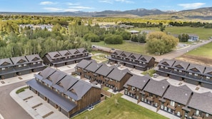 Ein moderner Wohnkomplex mit mehrstöckigen Gebäuden, einem zentralen Innenhof und Blick auf eine gebirgige Landschaft.