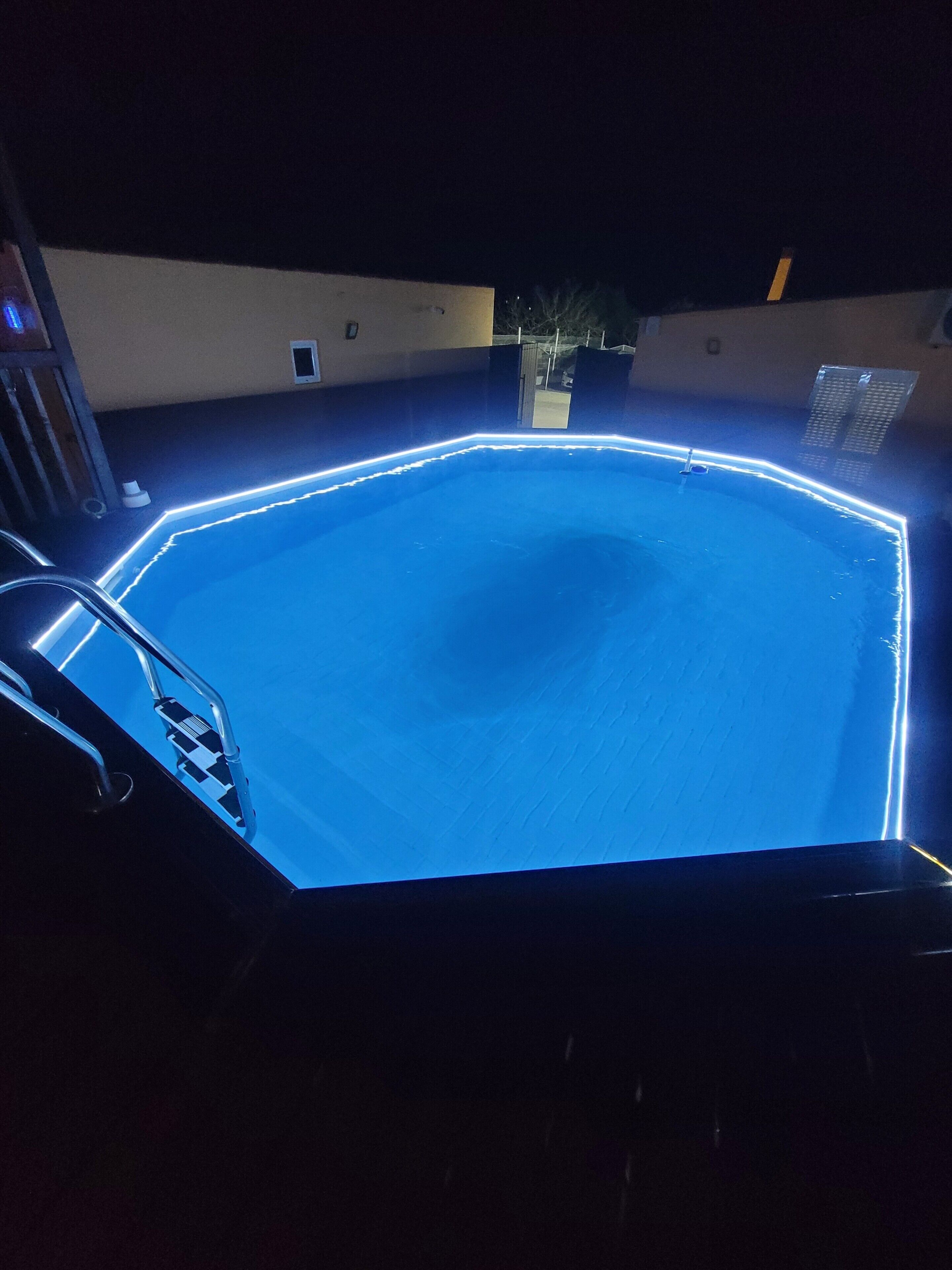 A swimming pool with a metal ladder and a lighted edge.