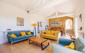 A living room with a blue sofa, a yellow sofa, a wooden coffee table, and a blue armchair. There is a fireplace, a lamp, and a painting on the wall. - Mas du Soleil  | 20m Pool & Sea View (Tourrettes-sur-Loup)