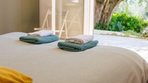 Ein Bett mit zwei gefalteten Handtüchern, einem Stuhl und Blick auf Grünfläche.