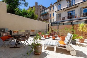 Une terrasse extérieure avec une table, des chaises, un fauteuil et des plantes en pot.