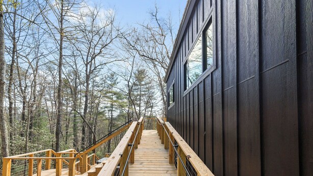 A wooden staircase leading to a building with a dark exterior, surrounded by trees. - BRAND NEW Modern Luxe Scandinavian Cabin with Hot tub/Fire Pit WIFI (Blue Ridge)