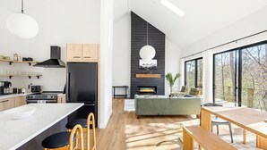 A modern kitchen with a large island, a dining area with a wooden table and benches, and a living space with a sofa and fireplace. - BRAND NEW Modern Luxe Scandinavian Cabin with Hot tub/Fire Pit WIFI (Blue Ridge)